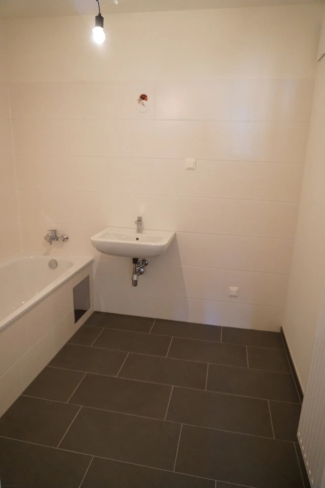 Leeres Badezimmer vor dem virtuellen Home Staging: Waschbecken, Badewanne, dunkle Bodenfliesen, weiße Wandfliesen.